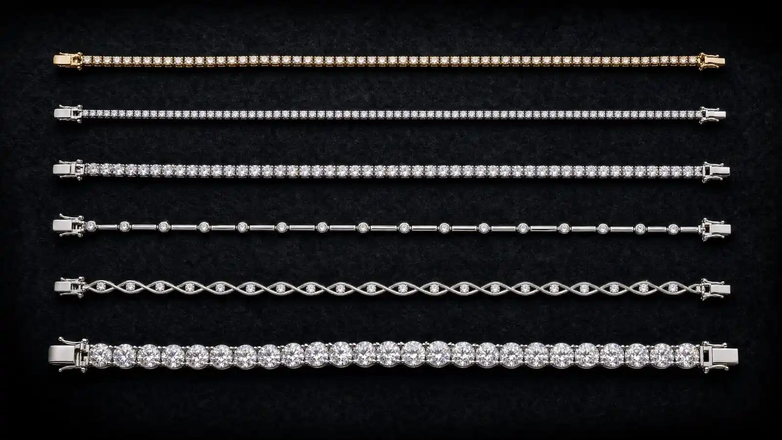 Six tennis bracelets of differing widths and metals arranged in parallel rows on dark charcoal velvet, from a fine 2mm line to a wide heavy white-gold line of large stones